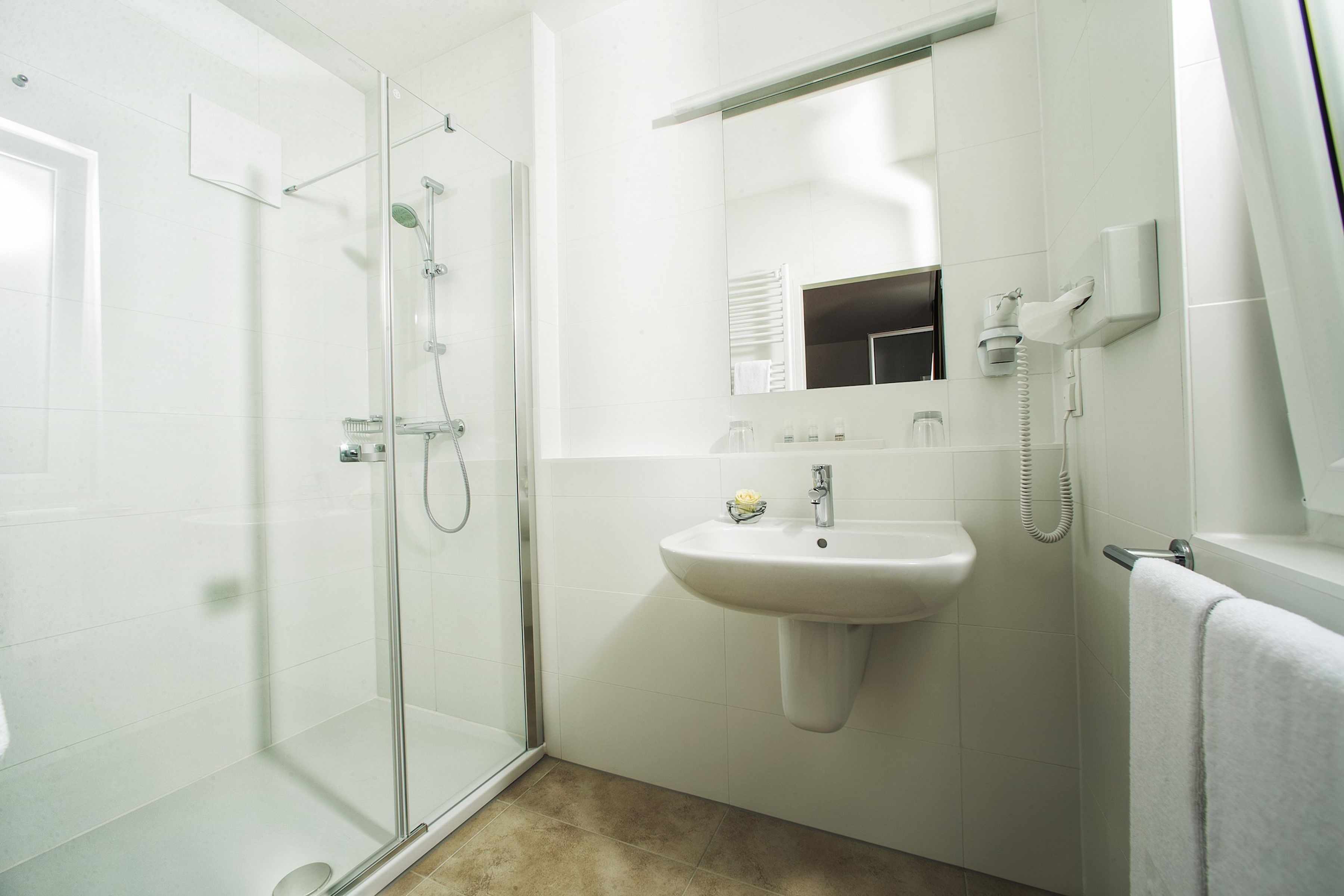 A modern bathroom with a glass shower enclosure, a pedestal sink, a mirror, and a towel rack.