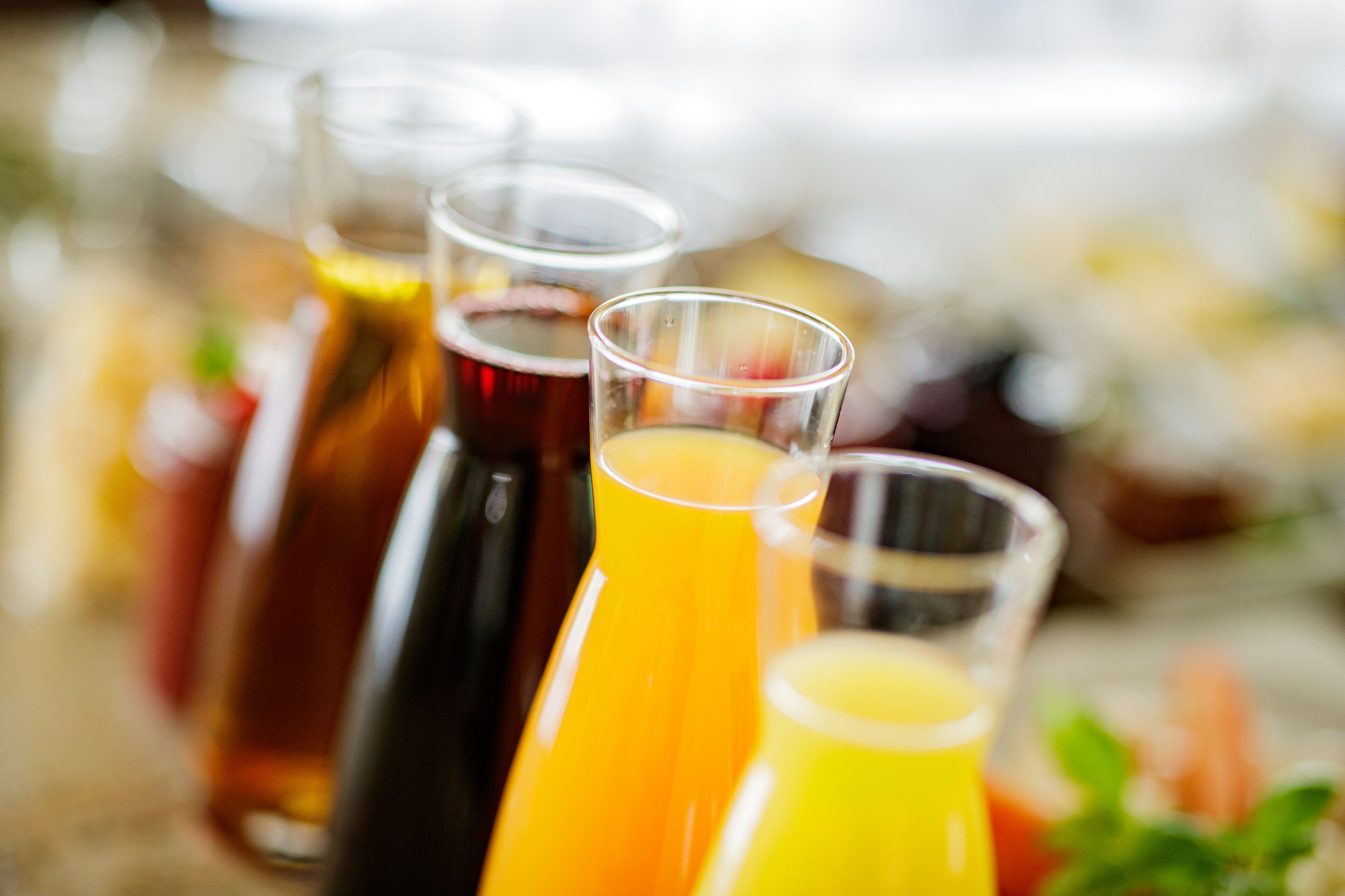 Diversas bebidas em diferentes recipientes, como copos e garrafas, com um fundo desfocado que sugere um ambiente social.