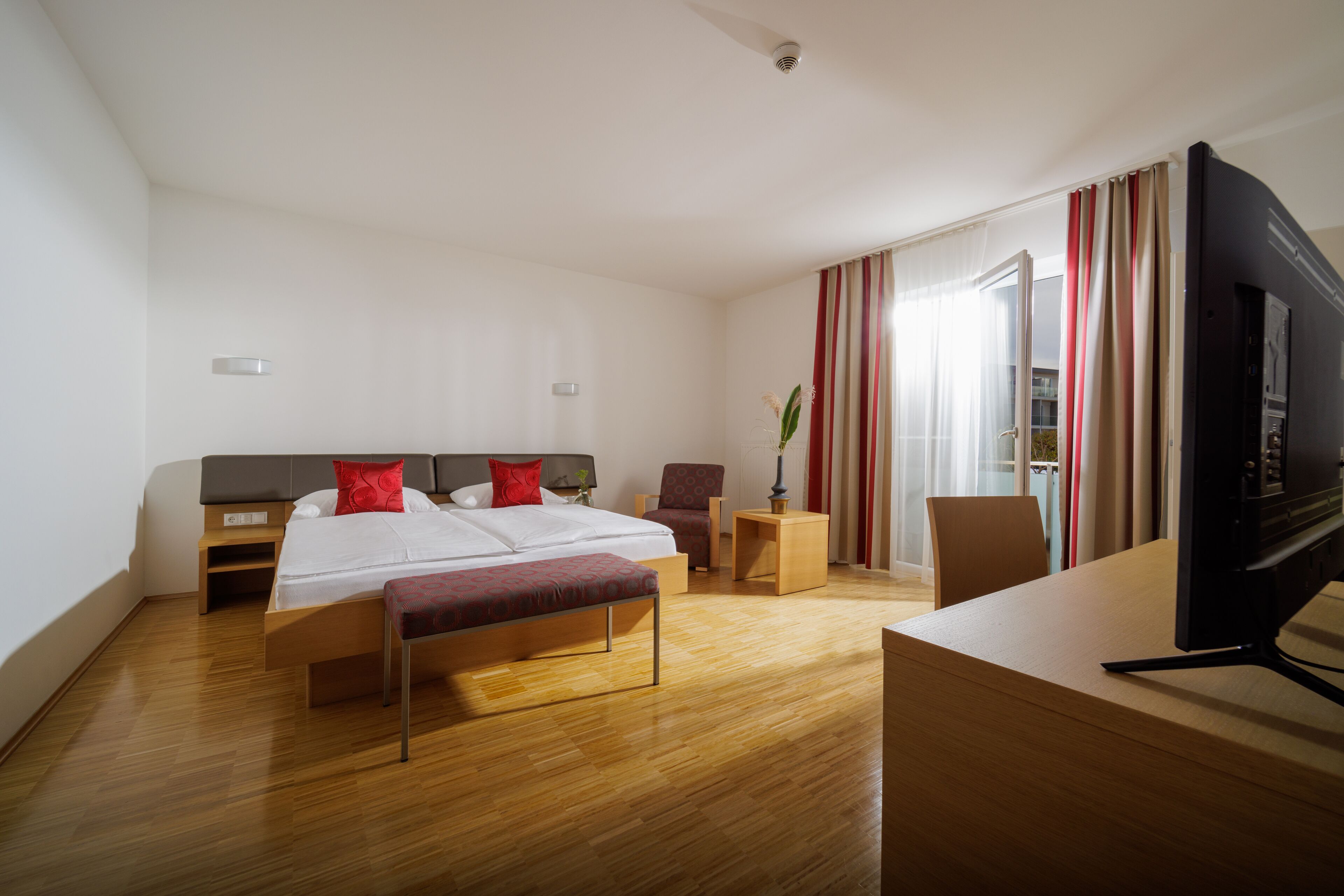 A hotel room with a bed, bedside tables, a desk with a computer, and a TV.