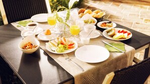 Une table mise pour le petit-déjeuner, avec différents plats, des boissons et un arrangement floral au centre.