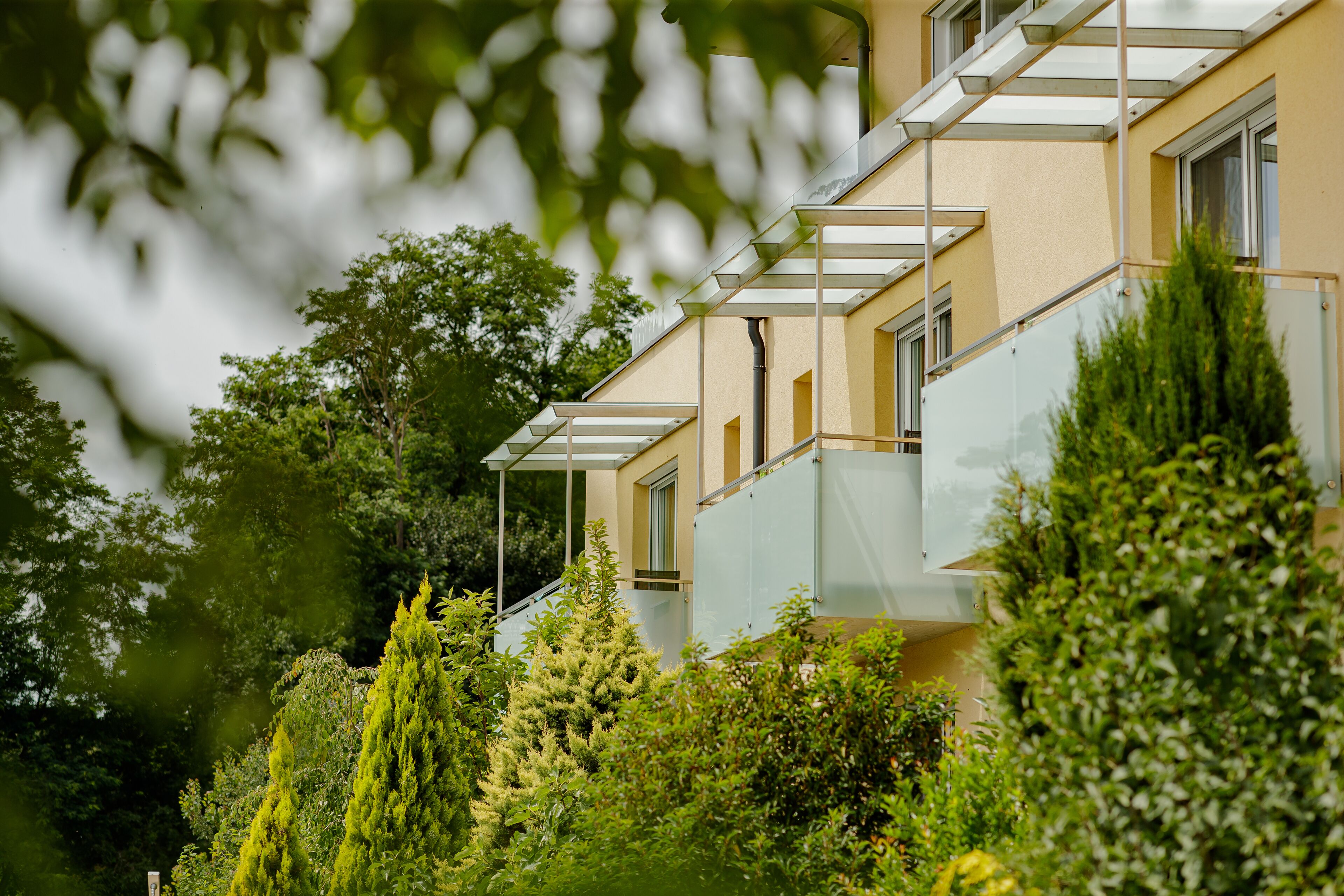 A multi-story building with balconies, surrounded by lush greenery.