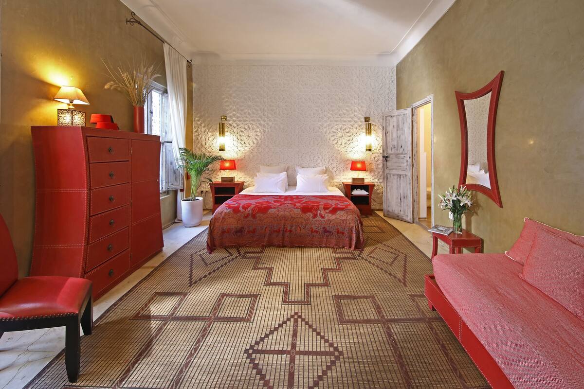 A bedroom with a bed, a red dresser, a red sofa, and two bedside tables with lamps.