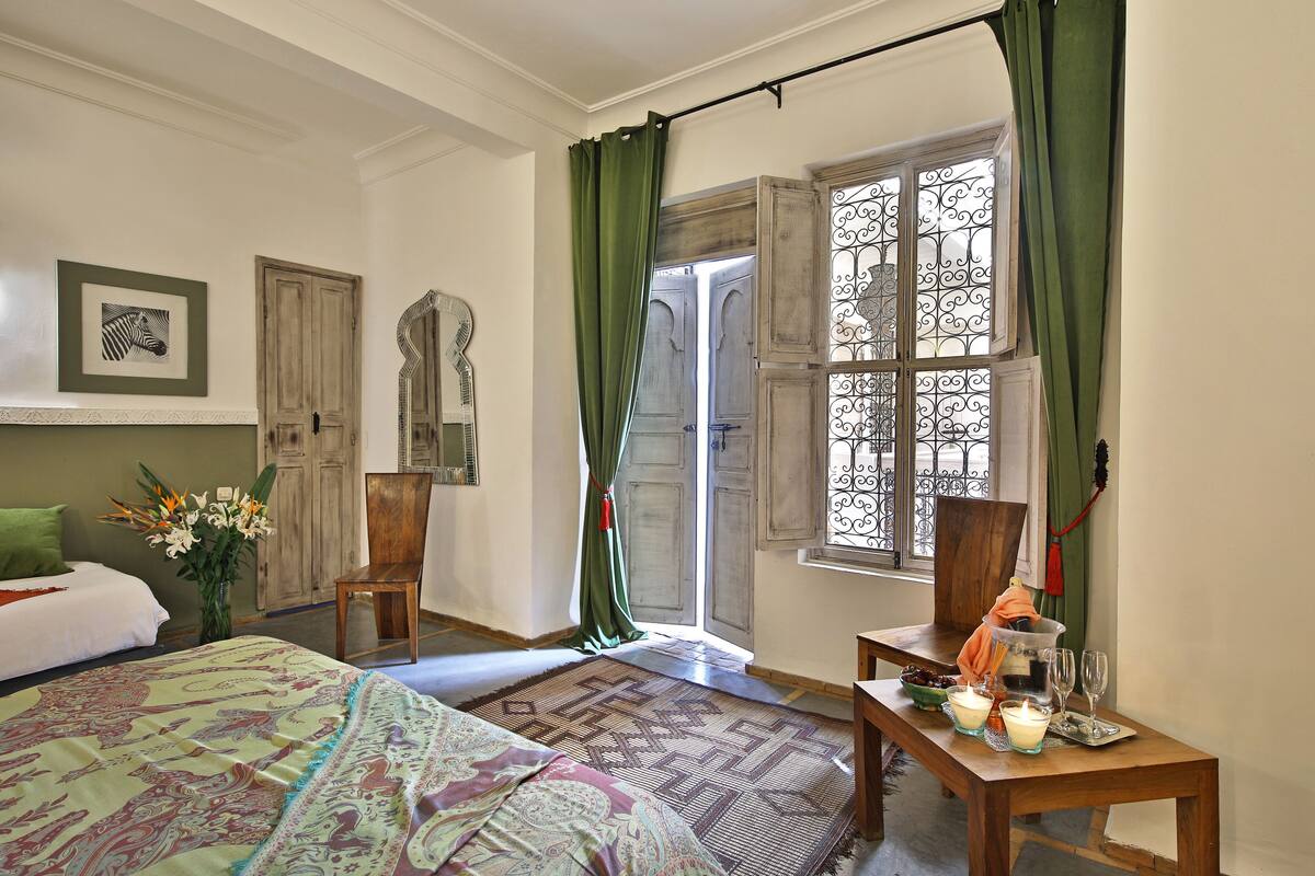A bedroom with a bed, a chair, a table with candles, and a window with curtains.