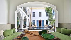 Ein modernes Interieur mit einer zentralen Sitzecke, einem Pool und Blick auf ein traditionelles Gebäude mit blauen Fensterläden.