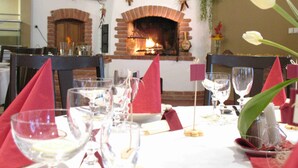 Un coin repas agrémenté d’une cheminée en briques, de tables dressées avec des serviettes et des verres rouges, et d’une tulipe dans un vase.