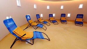 Une pièce dotée de plusieurs fauteuils de couleur bleue et orange, disposés en demi-cercle, et de petites fenêtres sur les murs.