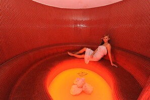 A person sitting inside a red brick-walled room with a yellow circular area at the bottom. - Hotel Cingov (Smizany)