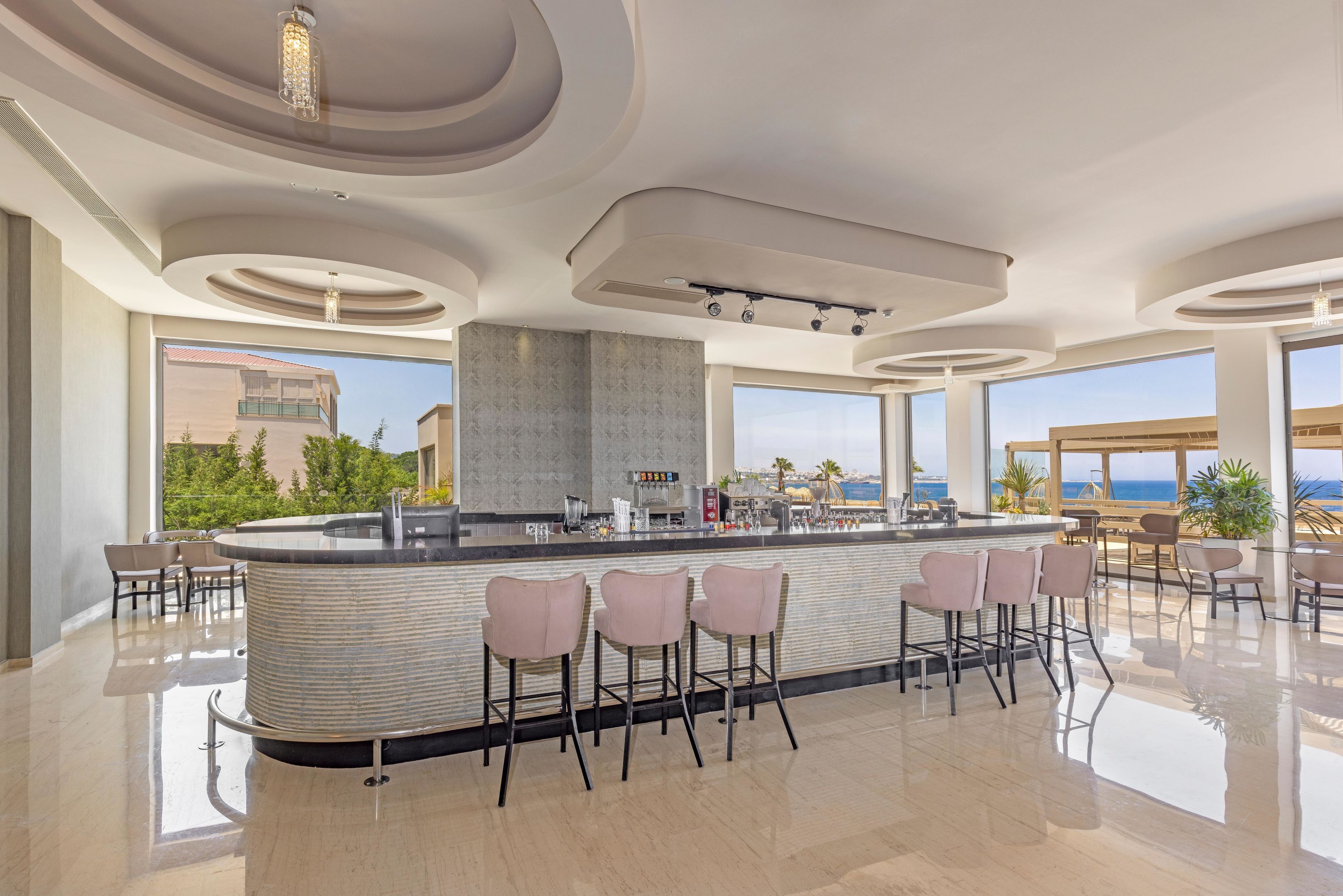 A modern bar area with a curved counter, bar stools, and large windows offering a view of the ocean.