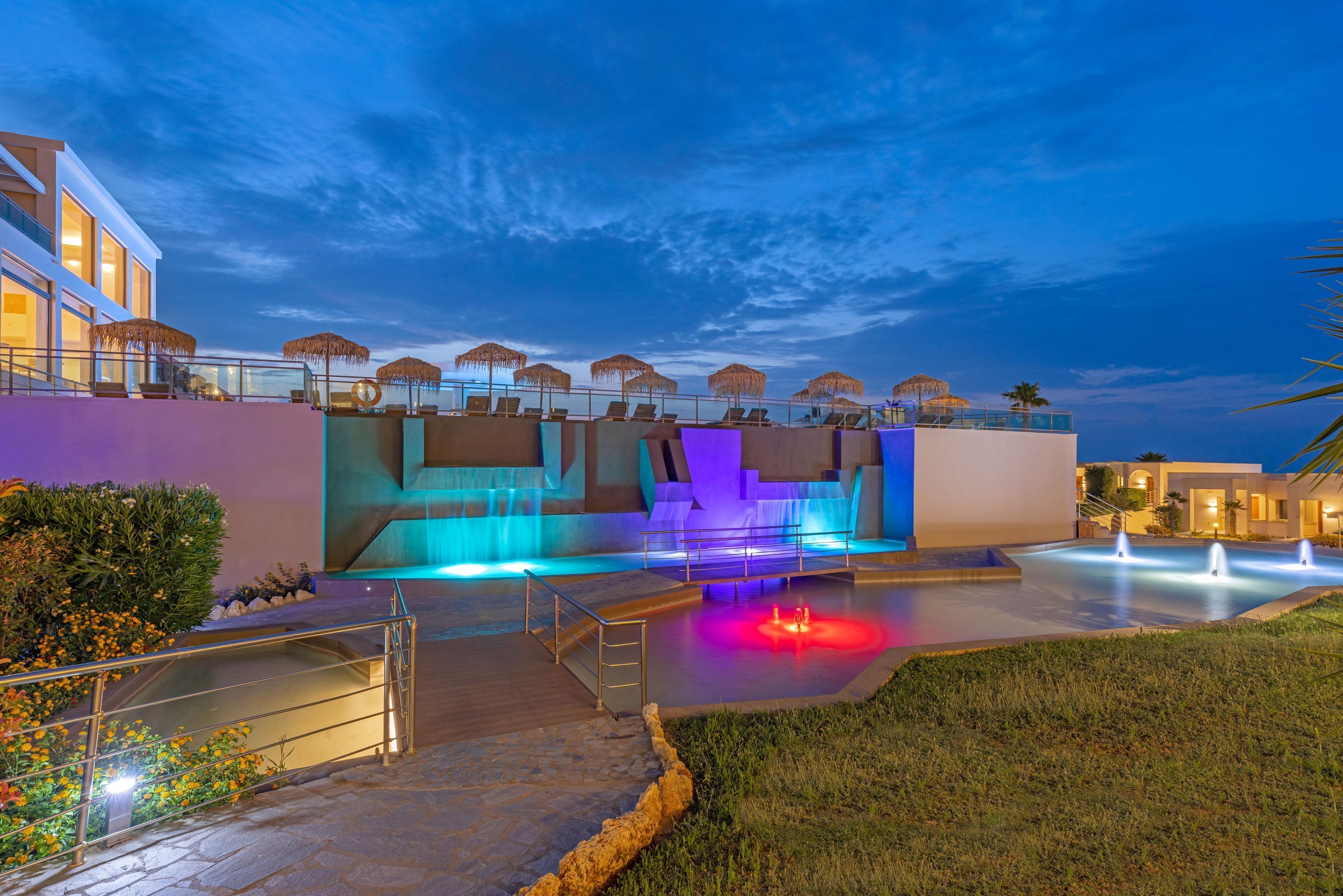 Un hotel modern amb zona de piscina, mobiliari exterior i entrada ben il·luminada.
