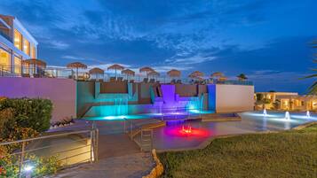Un hotel modern amb zona de piscina, mobiliari exterior i entrada ben il·luminada.