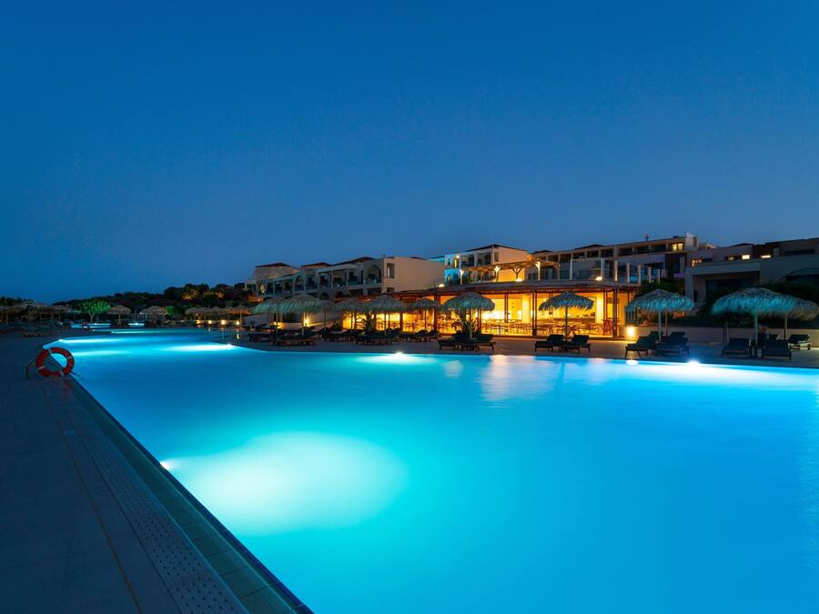 Una piscina con sillas de descanso y sombrillas, rodeada de edificios con balcones y terrazas.