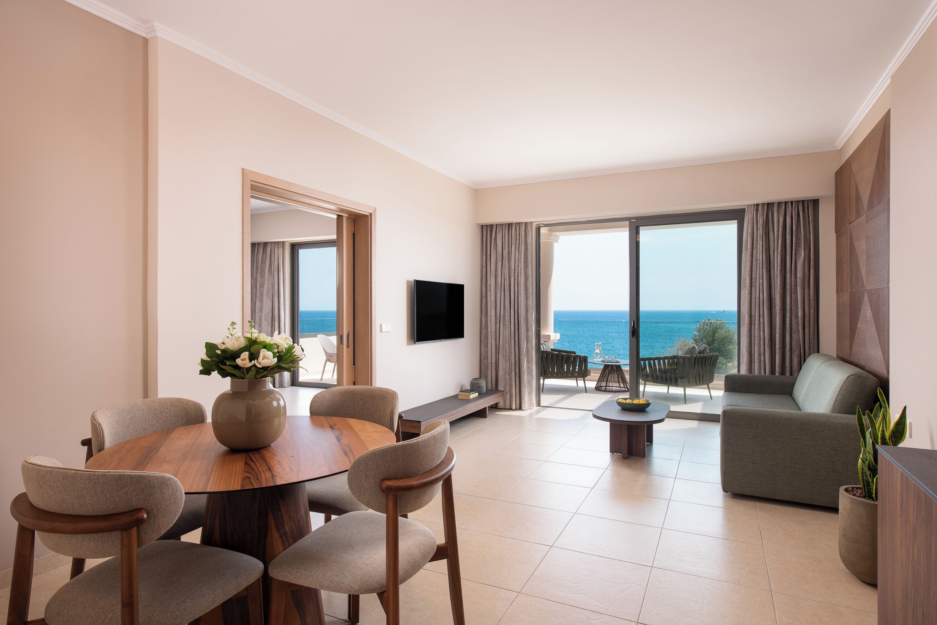 Una sala de estar moderna con una mesa de comedor de madera, asientos cómodos, un televisor de pantalla plana y un ventanal con vista al mar.