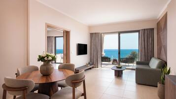 Una sala de estar moderna con una mesa de comedor de madera, asientos cómodos, un televisor de pantalla plana y un ventanal con vista al mar.