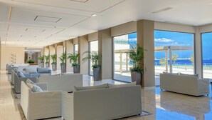 Un vestíbulo espacioso con mobiliario moderno, amplias ventanas con vistas al océano y un alto techo con iluminación empotrada.