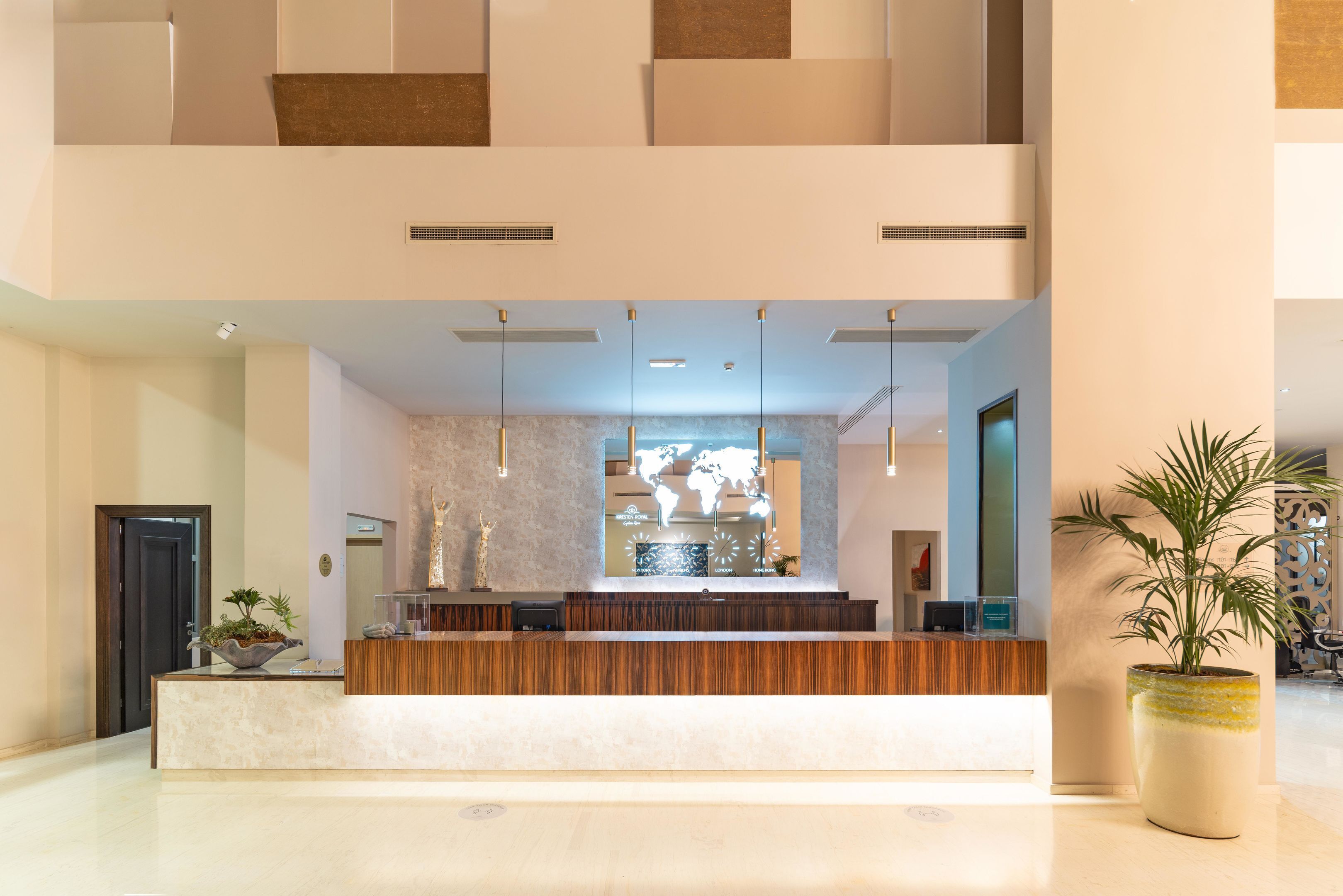 Un espace d’accueil moderne, avec un comptoir de réception en bois, une grande plante en pot et une carte du monde accrochée au mur.
