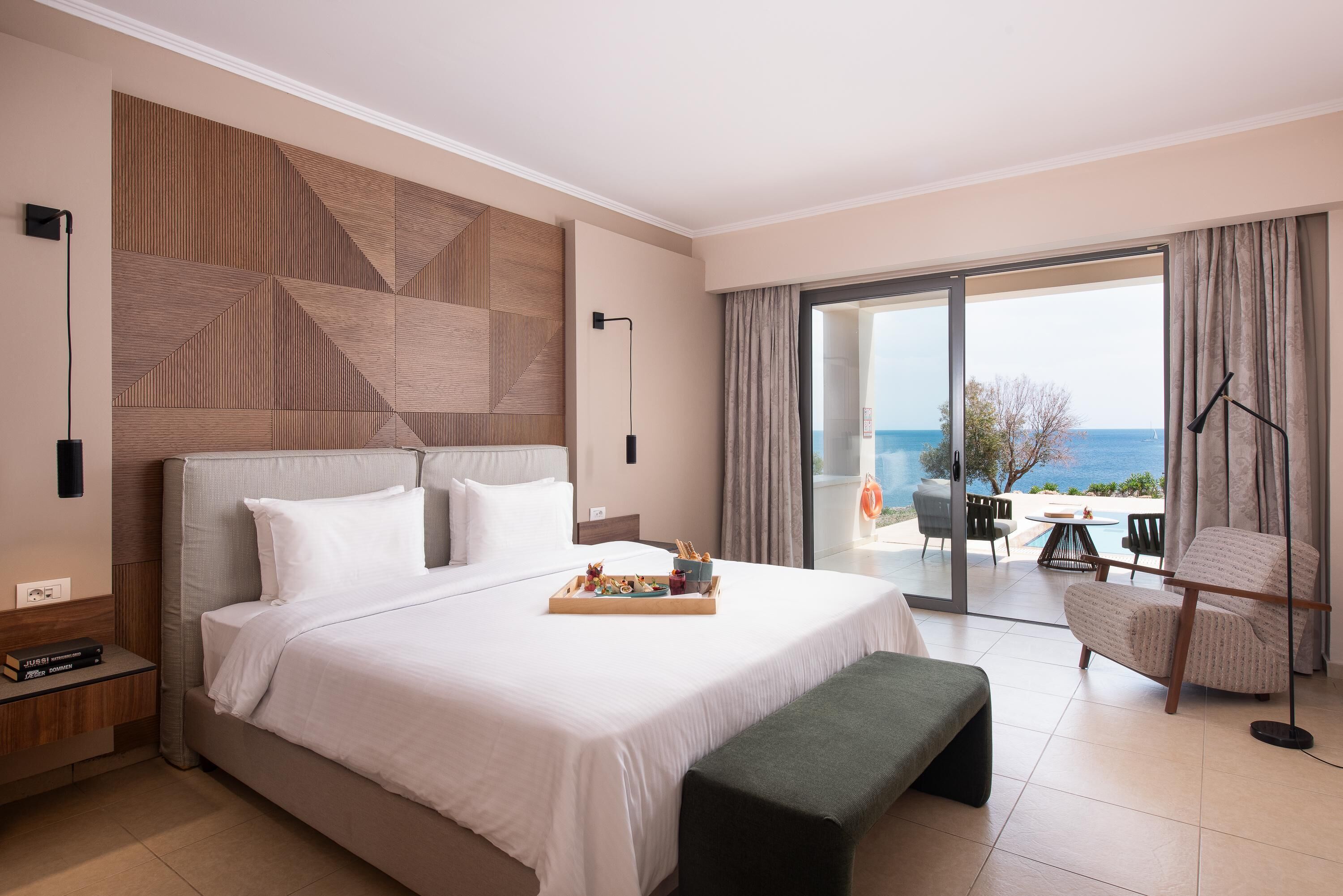 A hotel room with a large bed, a view of the sea, a balcony with outdoor seating, and a modern design.