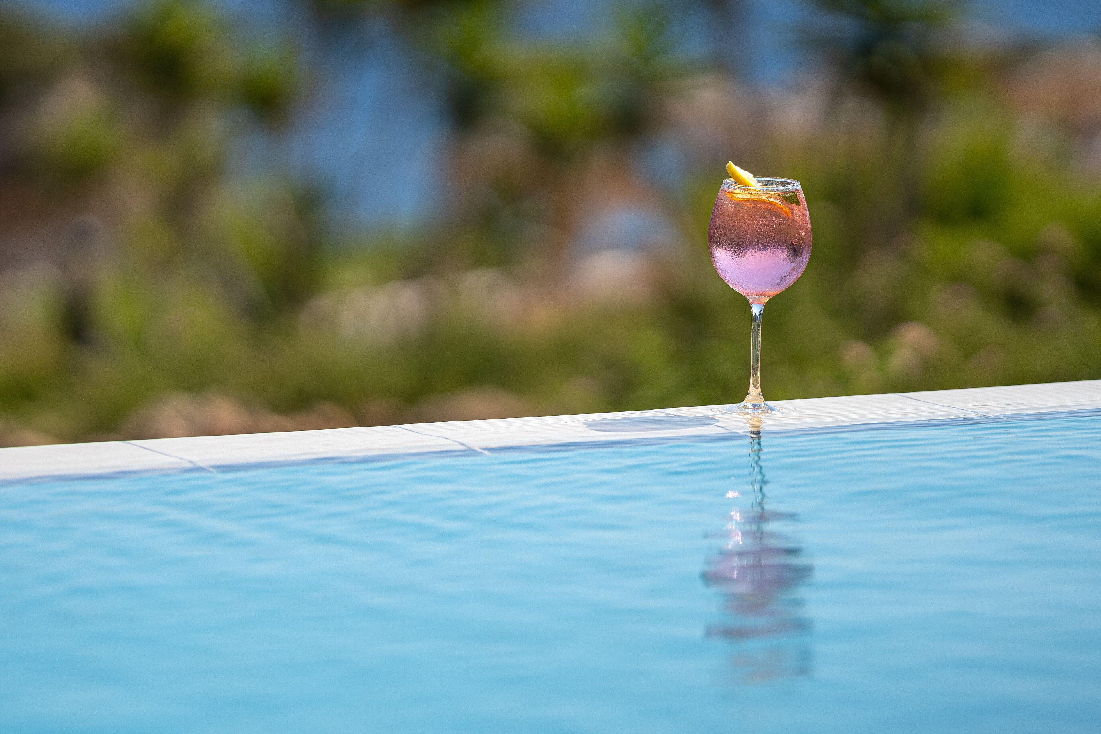 Un verre contenant une boisson et une tranche de citron, posé au bord d’une piscine.