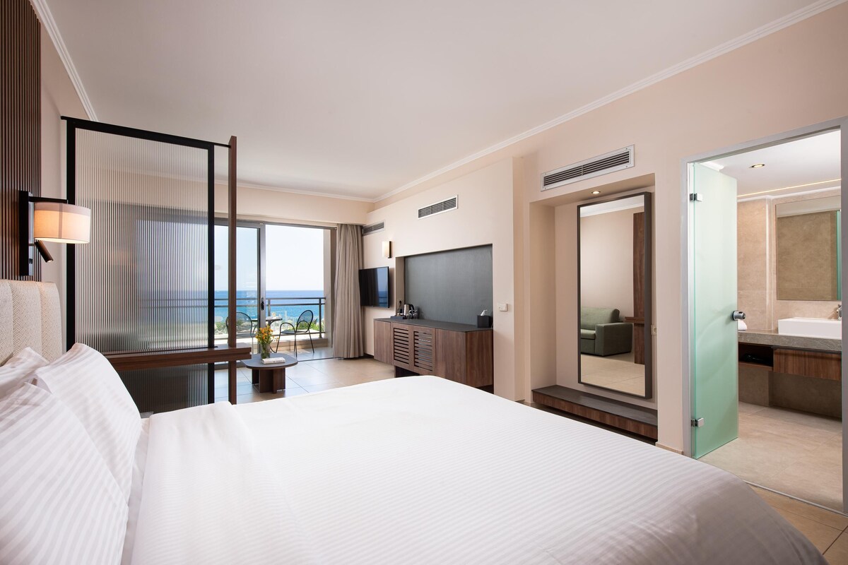 Une chambre d’hôtel moderne dotée d’un grand lit, d’une télévision, d’une salle de bain et offrant une vue sur l’océan.