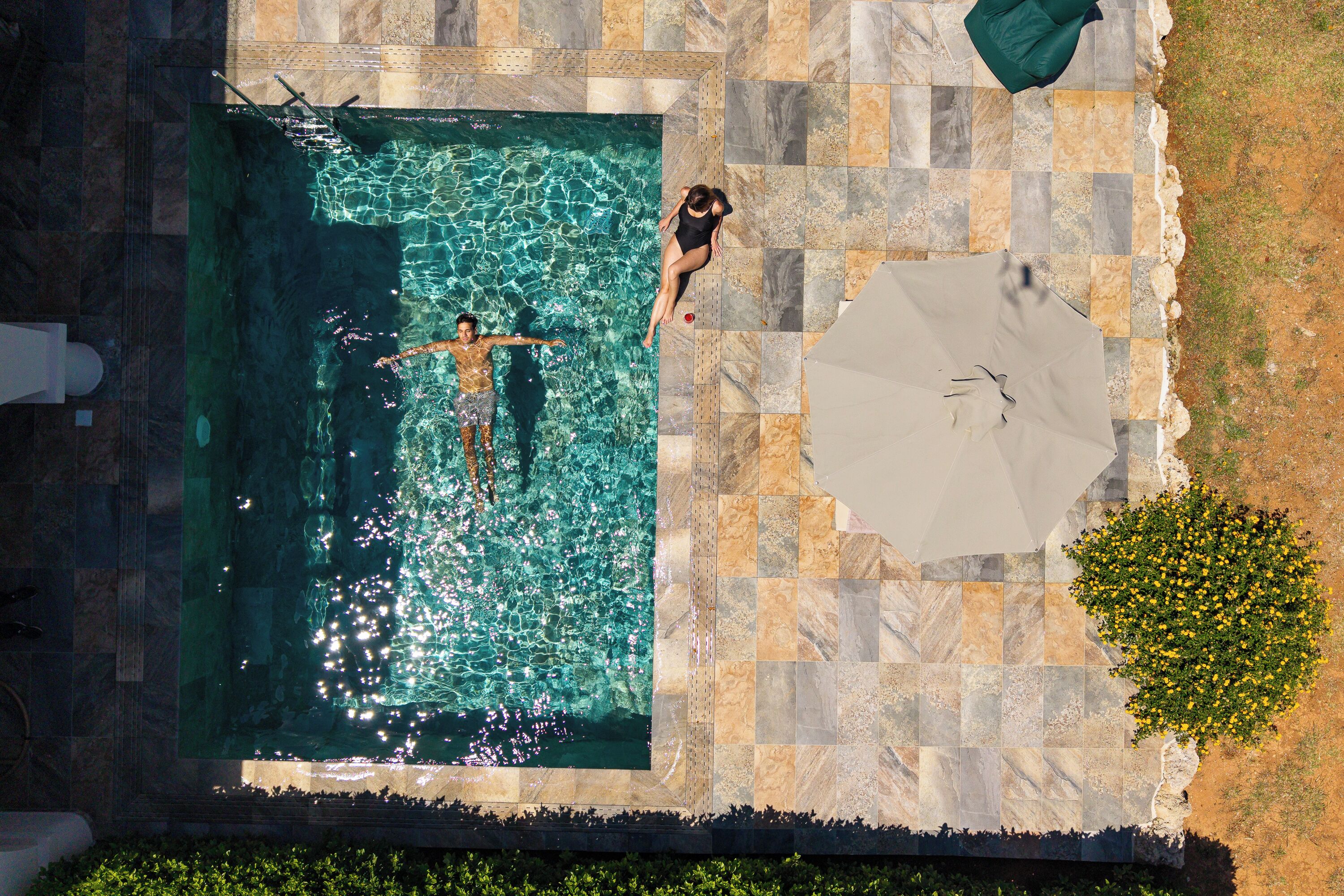 Une piscine à l’eau claire, entourée de carreaux de pierre et dotée d’un grand parasol.