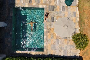 Una piscina con agua cristalina, rodeada de baldosas de piedra y un gran paraguas.