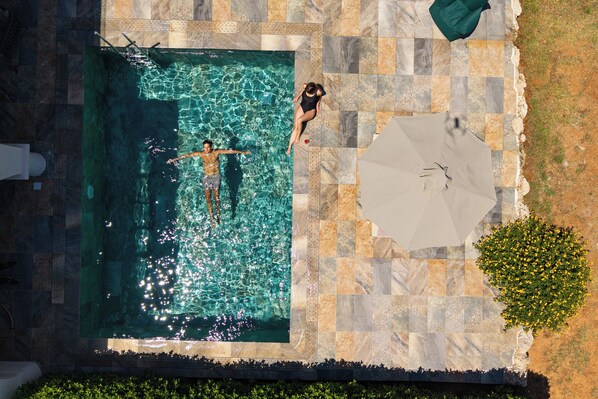 Una piscina con agua cristalina, rodeada de baldosas de piedra y un gran paraguas.