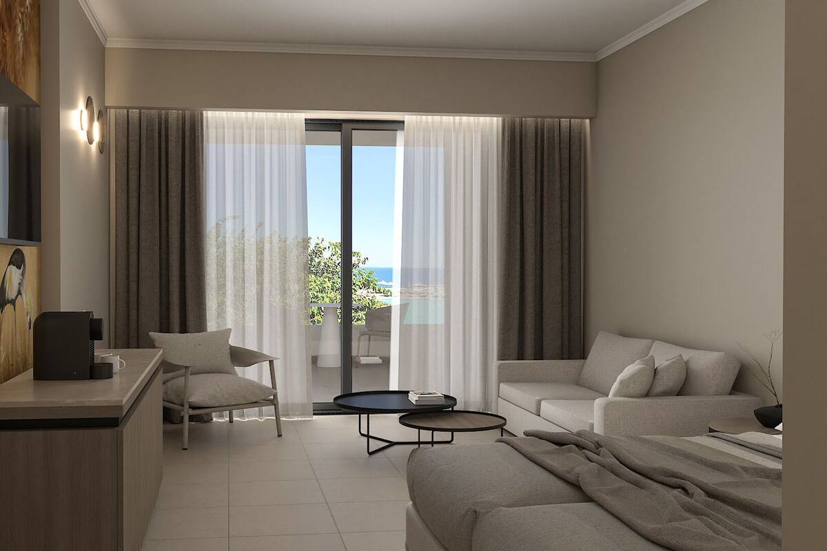 Een moderne hotelkamer met een bank, een klein bijzettafeltje, een televisie en een balkon met uitzicht op zee.