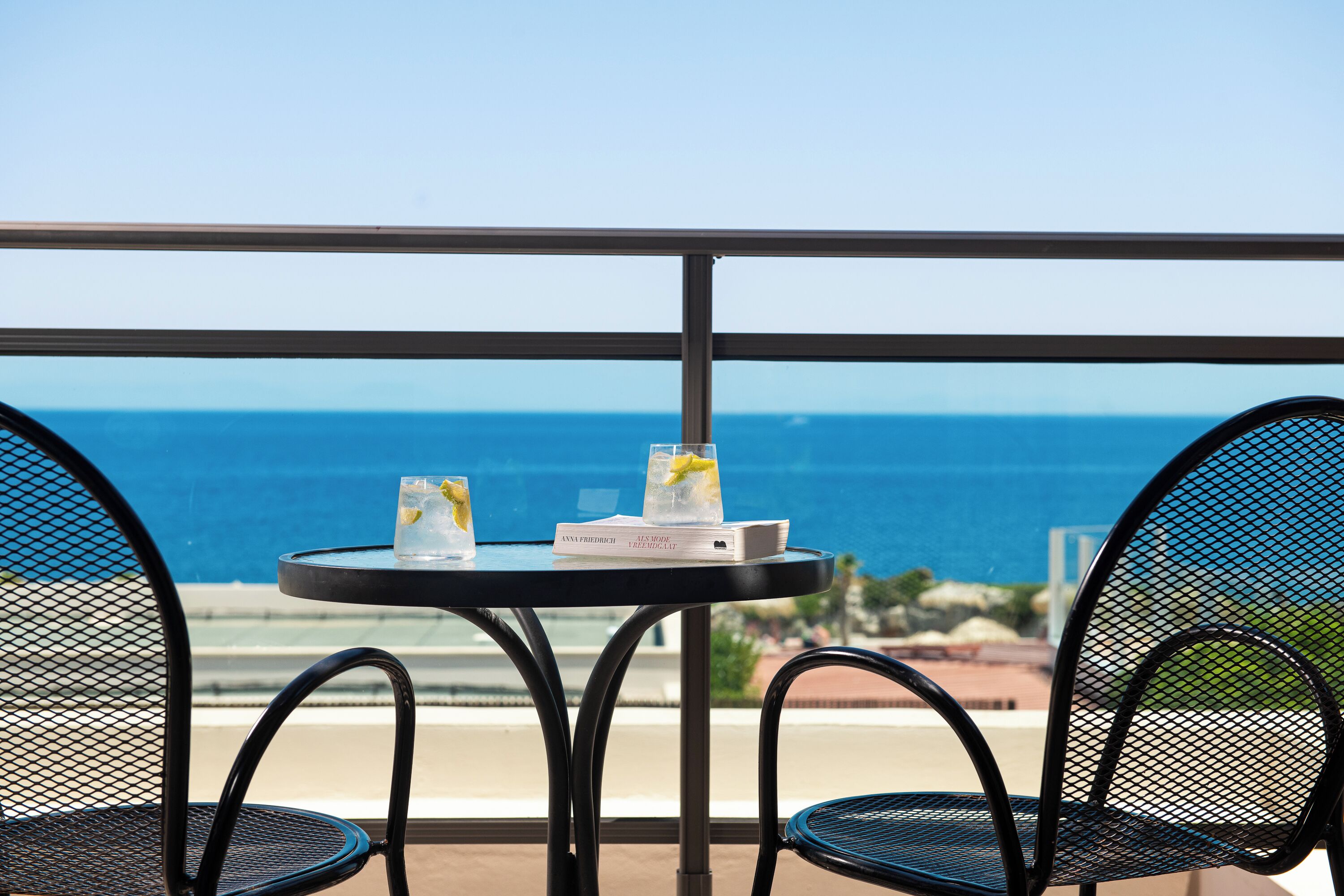 A balcony with two chairs and a table, a book, and a glass with a lemon slice.
