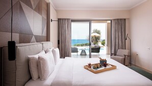 Habitación de hotel con una cama grande, vista al mar y un comedor con mesa y sillas.