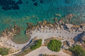 An aerial view of a beach with clear turquoise waters, rocky formations, and a row of sun loungers. - Kresten Royal Euphoria Resort (Rhodes)