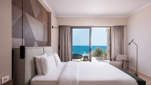 Habitación de hotel con una cama grande, vista al mar y un balcón con mesa y sillas.