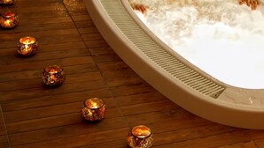 Una persona relajándose en un jacuzzi rodeado de velas y flores sobre un suelo de madera.