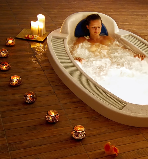 A person relaxing in a hot tub surrounded by candles and flowers on a wooden floor. - Kresten Royal Euphoria Resort (Rhodes)