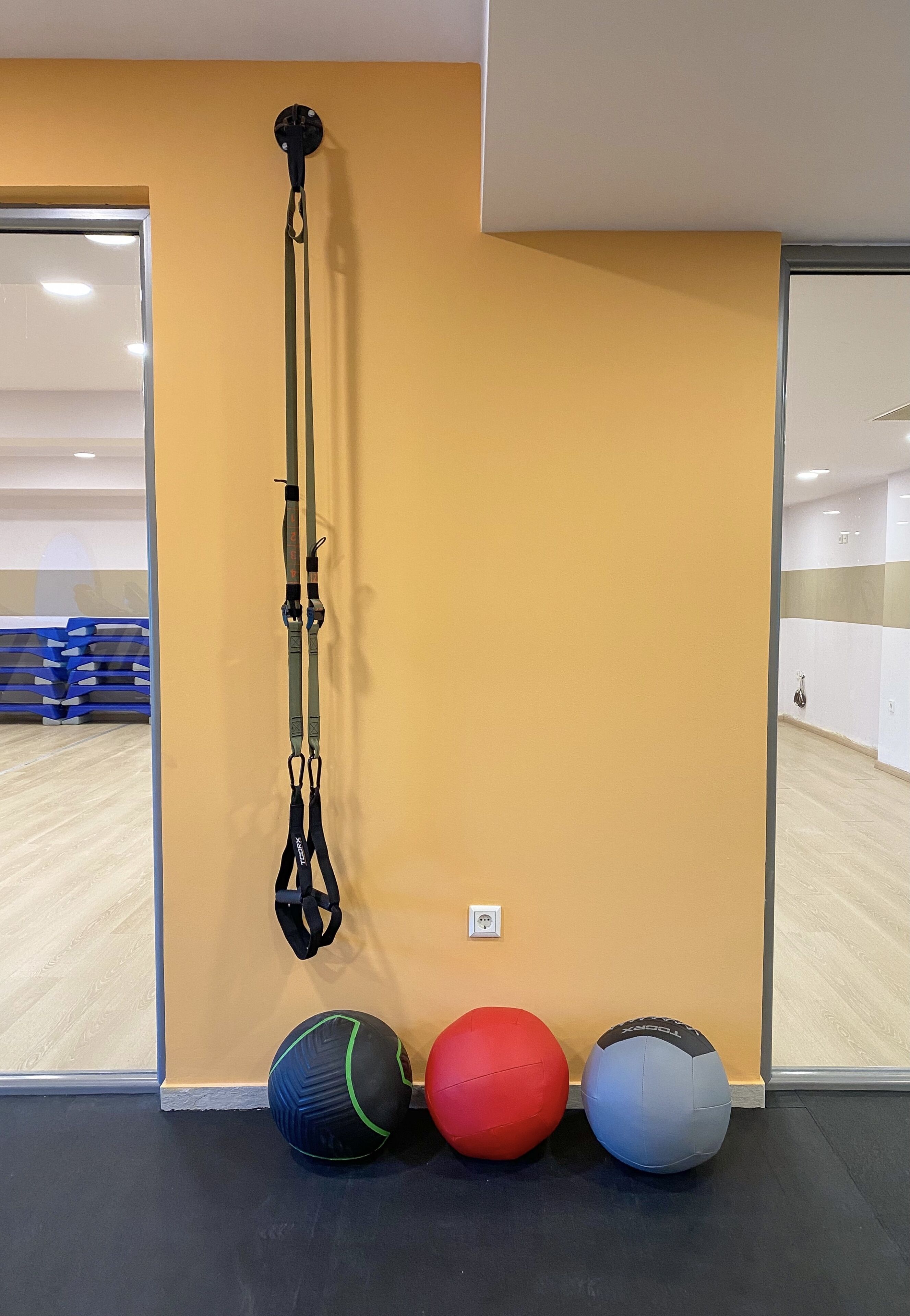 Una habitación con una pared amarilla, una banda de ejercicio negra y tres pelotas de ejercicio.