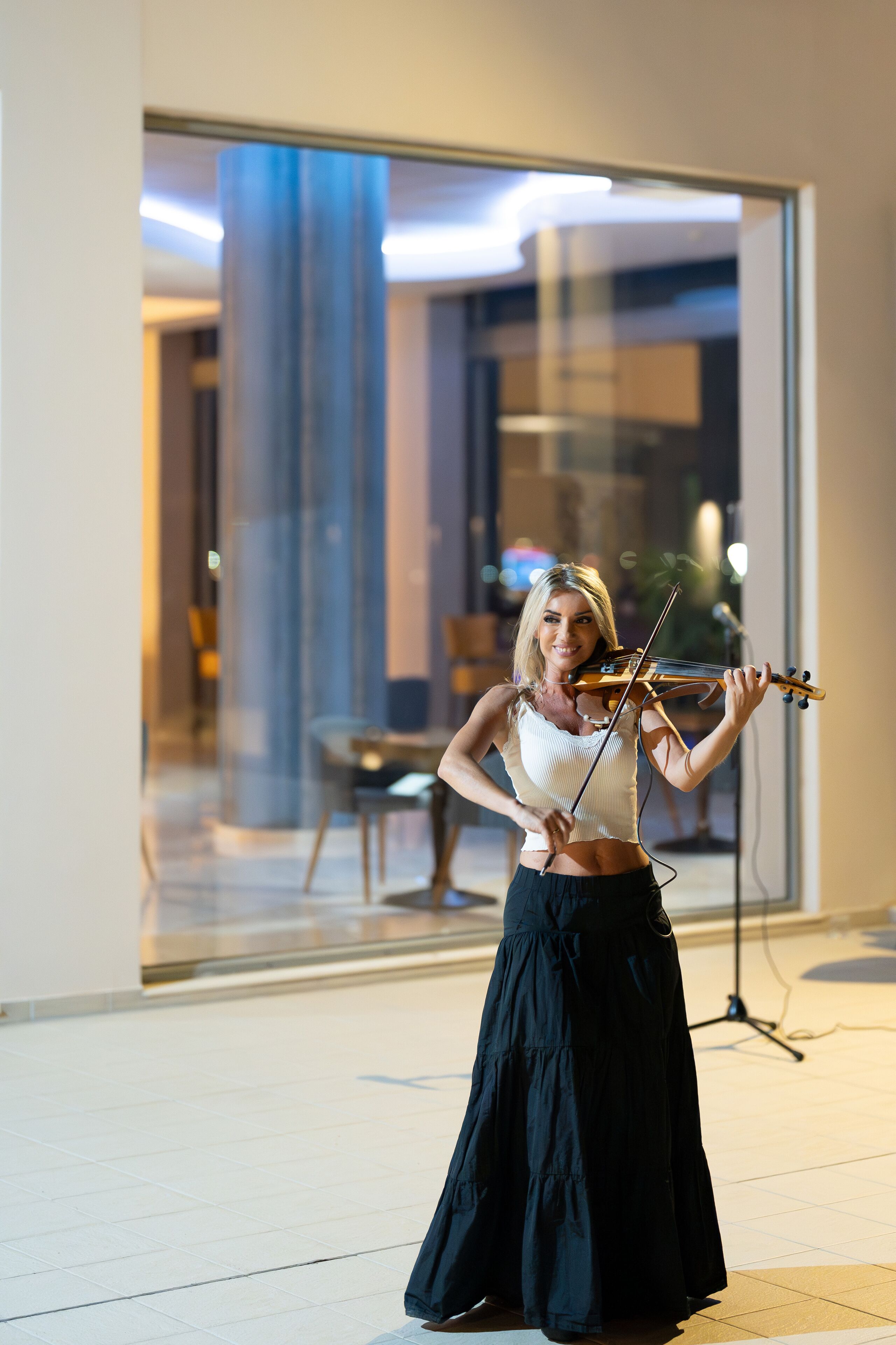Eine Person spielt Violine in einem modernen Innenraum mit einer Glaswand und einem sichtbaren Essbereich im Hintergrund.