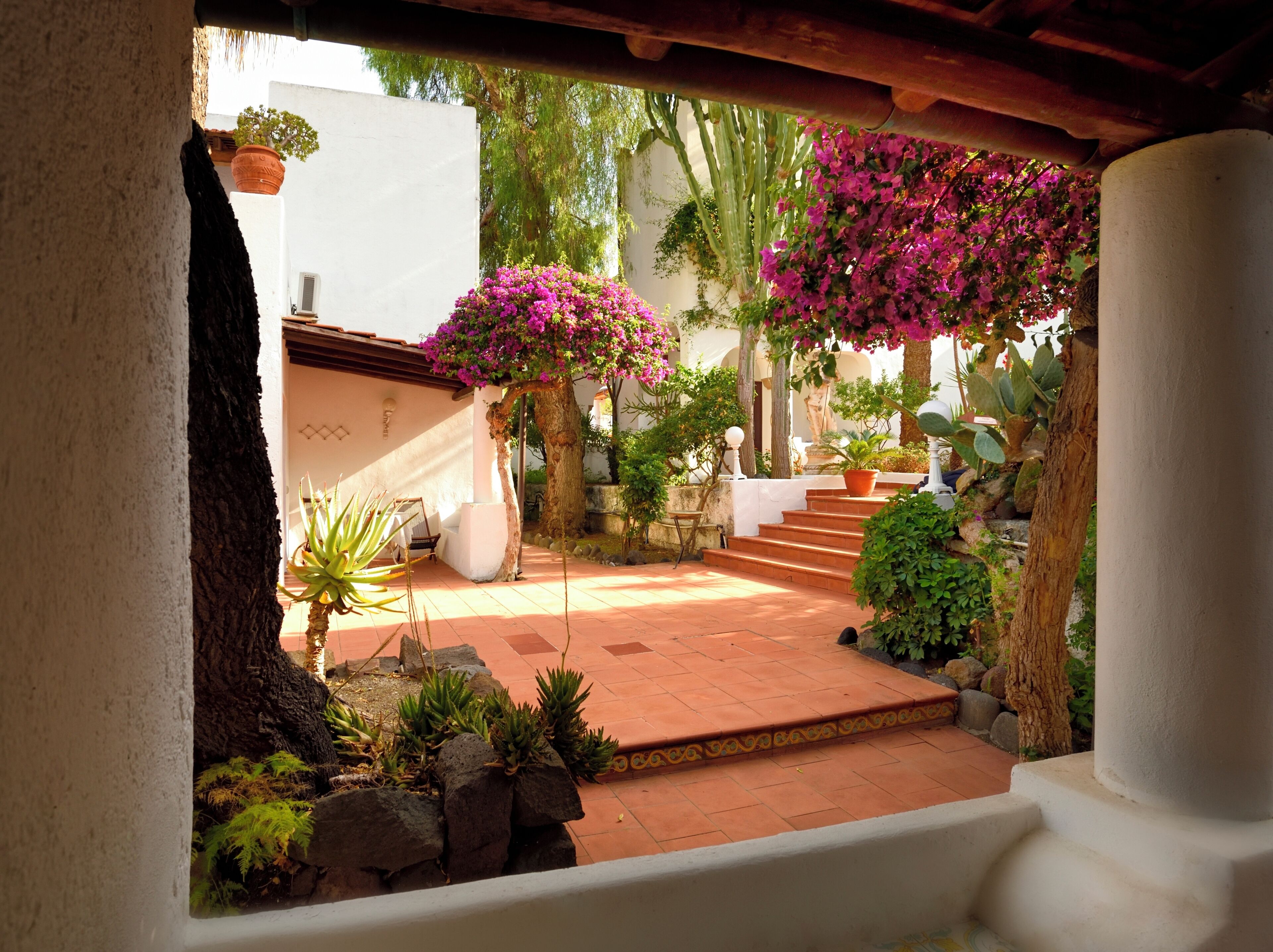 A courtyard with a tiled floor, a stone bench, and potted plants.