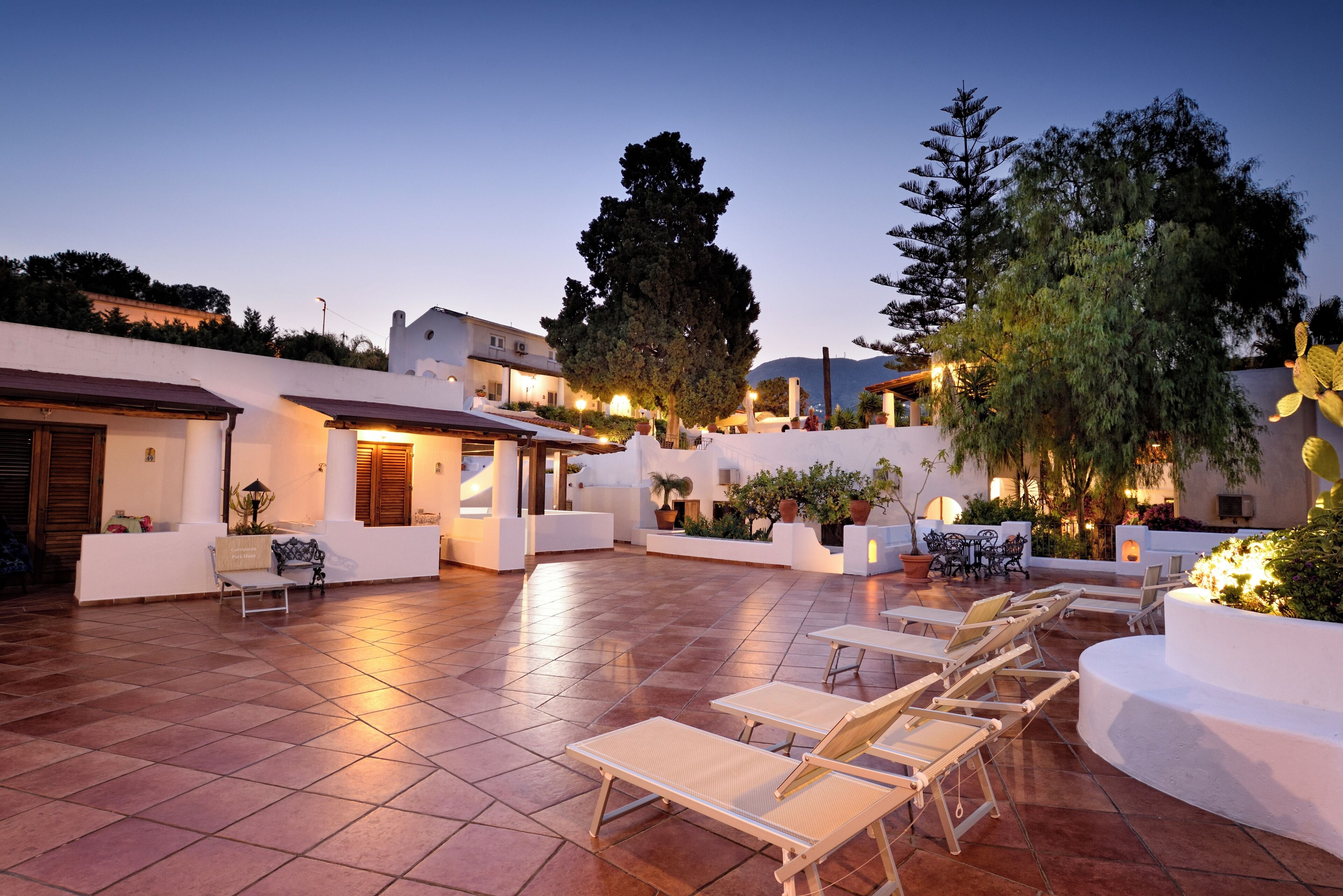 An outdoor patio with lounge chairs and tables, surrounded by white walls and potted plants.