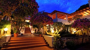 A well-lit staircase leading to a building with a covered patio area, surrounded by potted plants and flowering trees. - Gattopardo Park Hotel (Lipari)