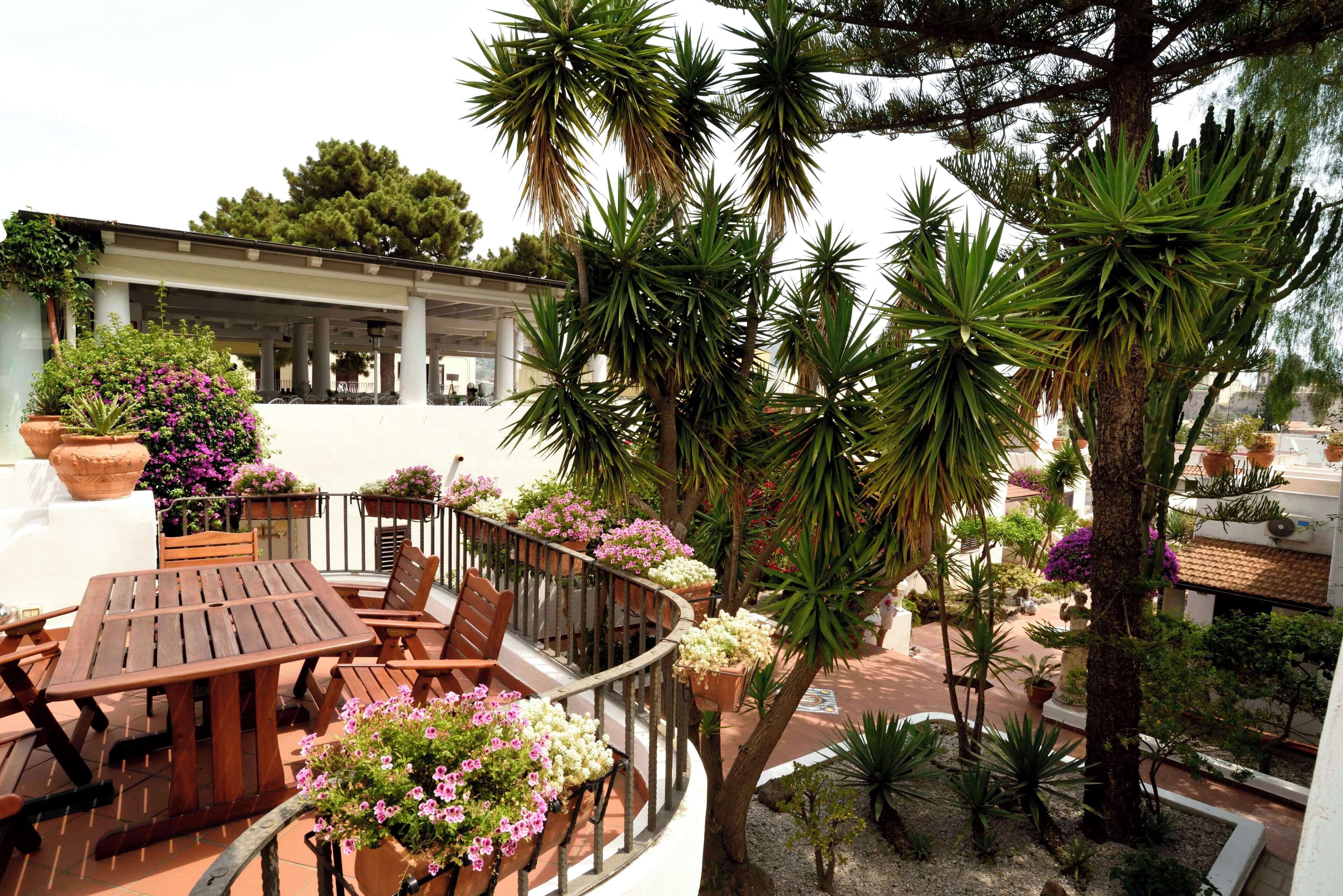 A balcony with wooden furniture, potted plants, and a view of a building with columns.