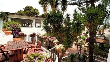 A balcony with wooden furniture, potted plants, and a view of a building with columns.