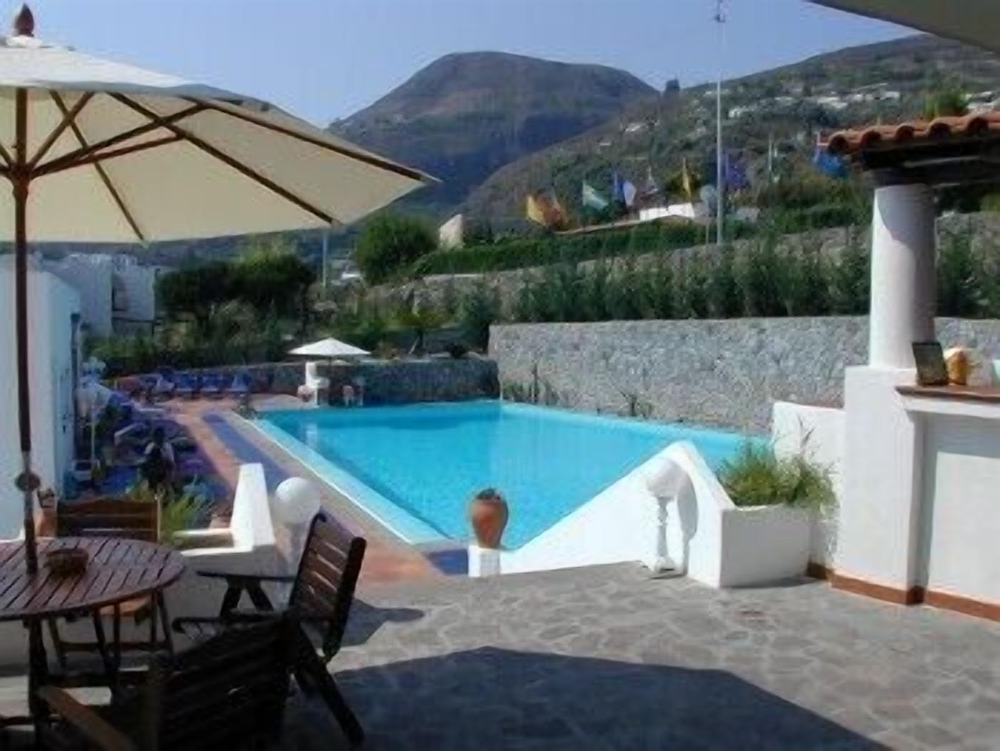 A swimming pool with a patio area, including a table and chairs, surrounded by a stone wall and a view of the mountains.