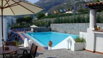 A swimming pool with a patio area, including a table and chairs, surrounded by a stone wall and a view of the mountains.