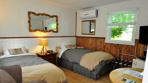 A hotel room with two beds, a wooden floor, a desk with a chair, a lamp, and a TV. - Motel Des Deux Lacs Inc (Shefford)
