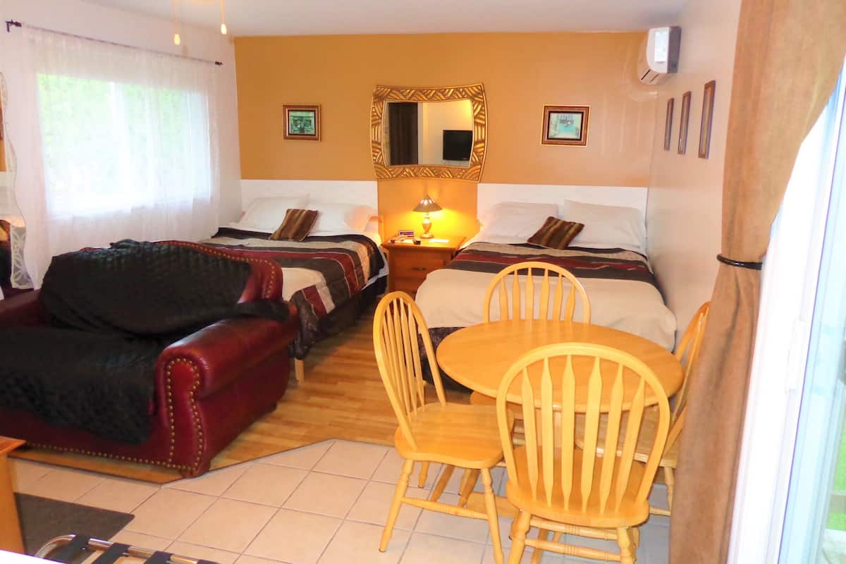 Ein Hotelzimmer mit zwei Betten, einem roten Sofa, einem Holzespeisesaal mit Stühlen und einem kleinen Tisch mit Lampe.