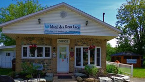 A small, two-story motel with a stone facade and a sign reading "Motel des Deux Lacs." - Motel Des Deux Lacs Inc (Shefford)