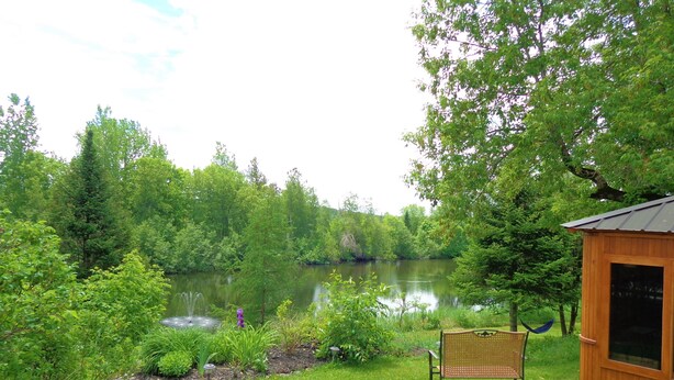 A lakeside patio with a wooden cabin, a table with chairs, and lush greenery. - Motel Des Deux Lacs Inc (Shefford)