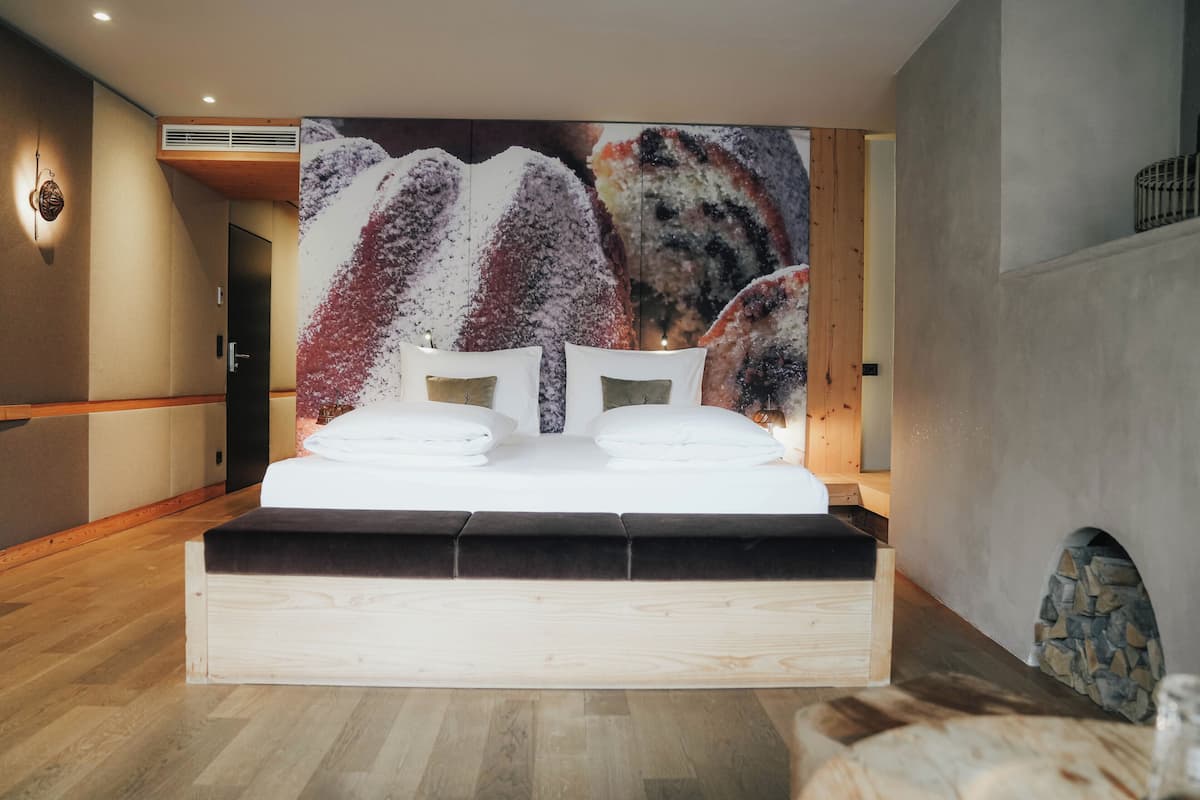 Quarto moderno com cama grande, cabeceira de madeira e parede de pedra.