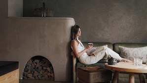 A person sitting on a couch by a fireplace, holding a cup. - Weisses Roessl Innsbruck GmbH (Innsbruck)