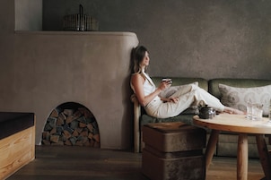 Una persona sentada en un sofá junto a una chimenea, sosteniendo una taza.