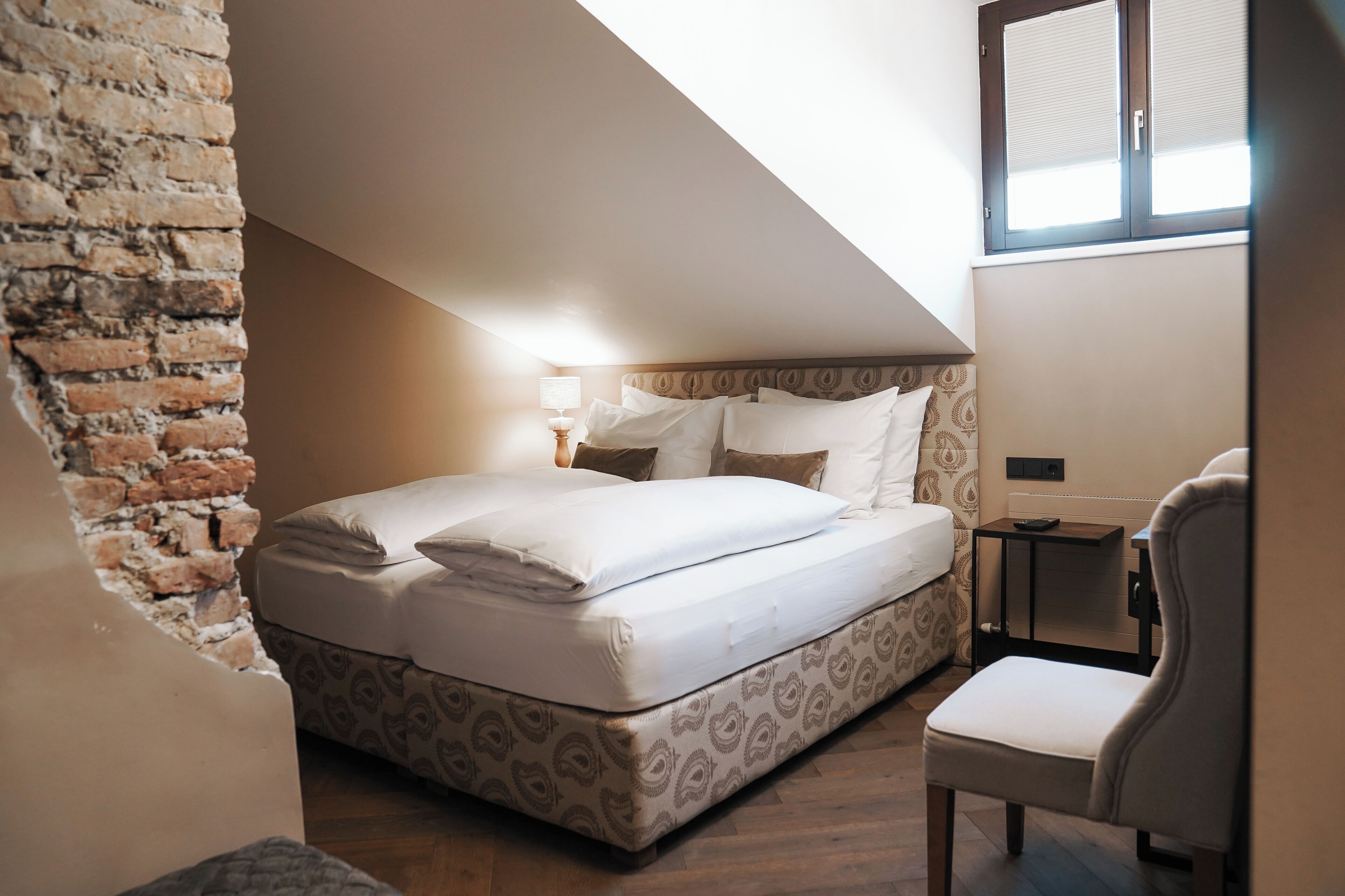 A bedroom with a bed, a chair, a nightstand, a lamp, and a window.