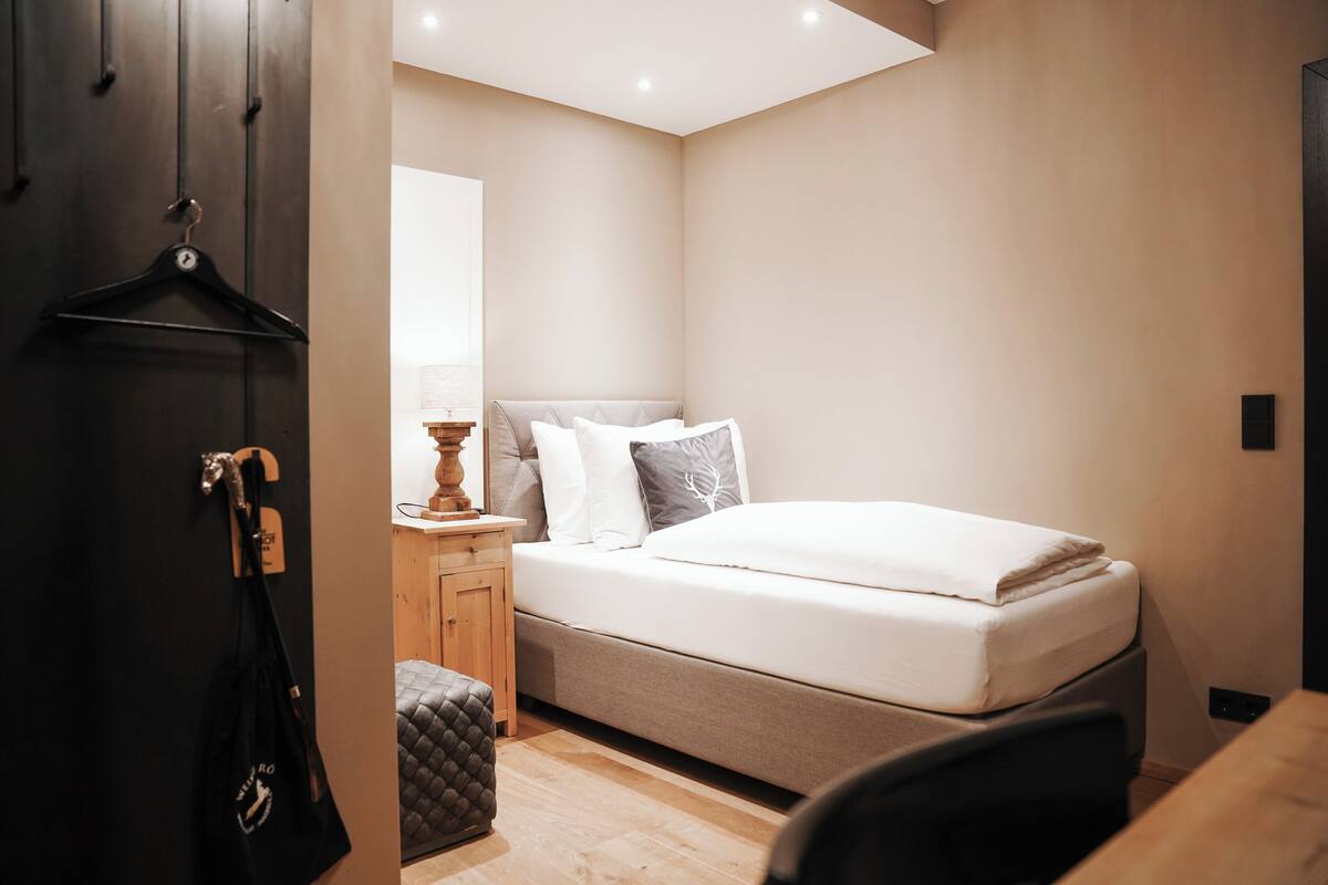 Quarto com cama, mesa de cabeceira, luminária e um saco pendurado.